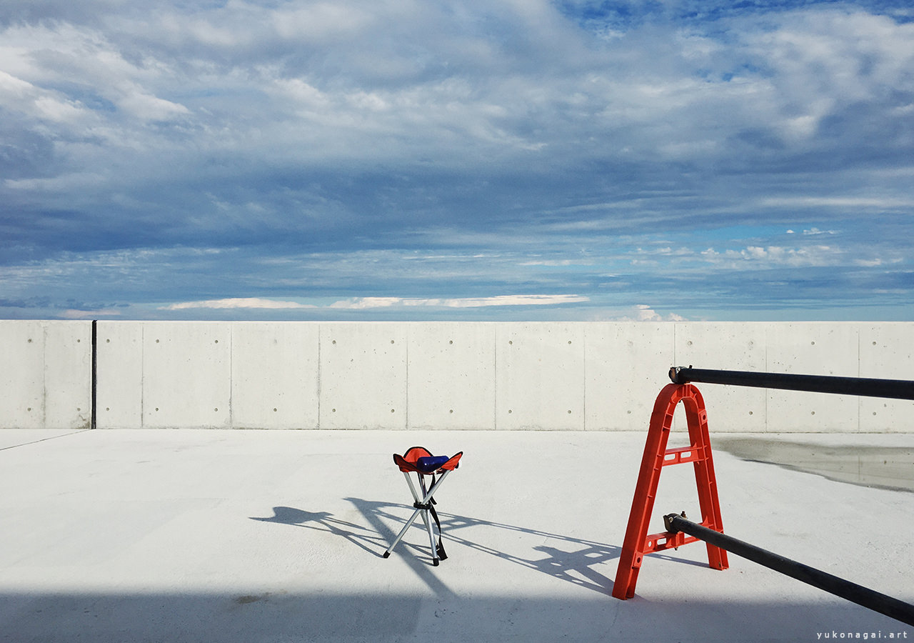 A folding stool on concrete under blue sky.