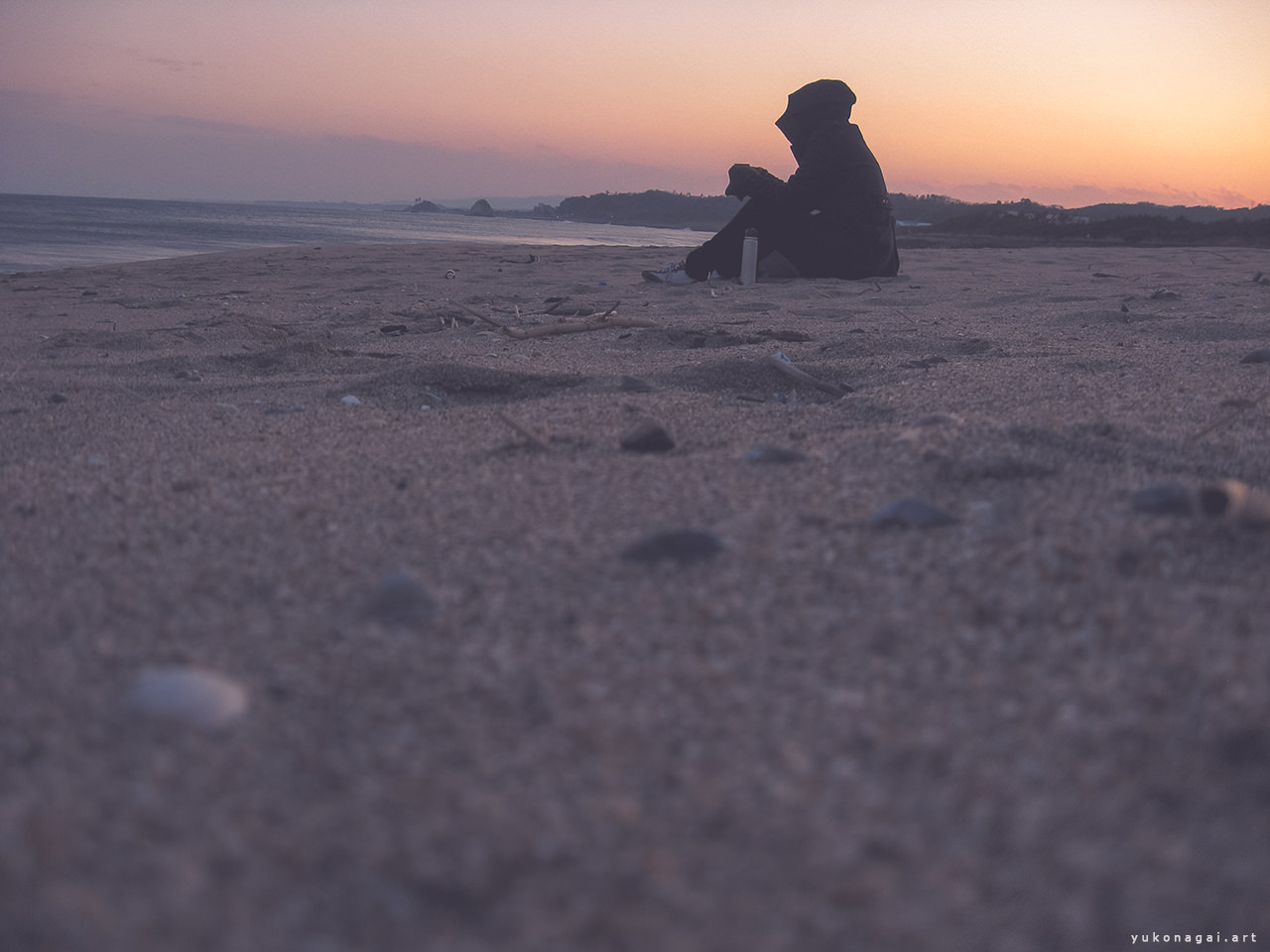 A silhouette of a person having a tea on the beach at sundown.