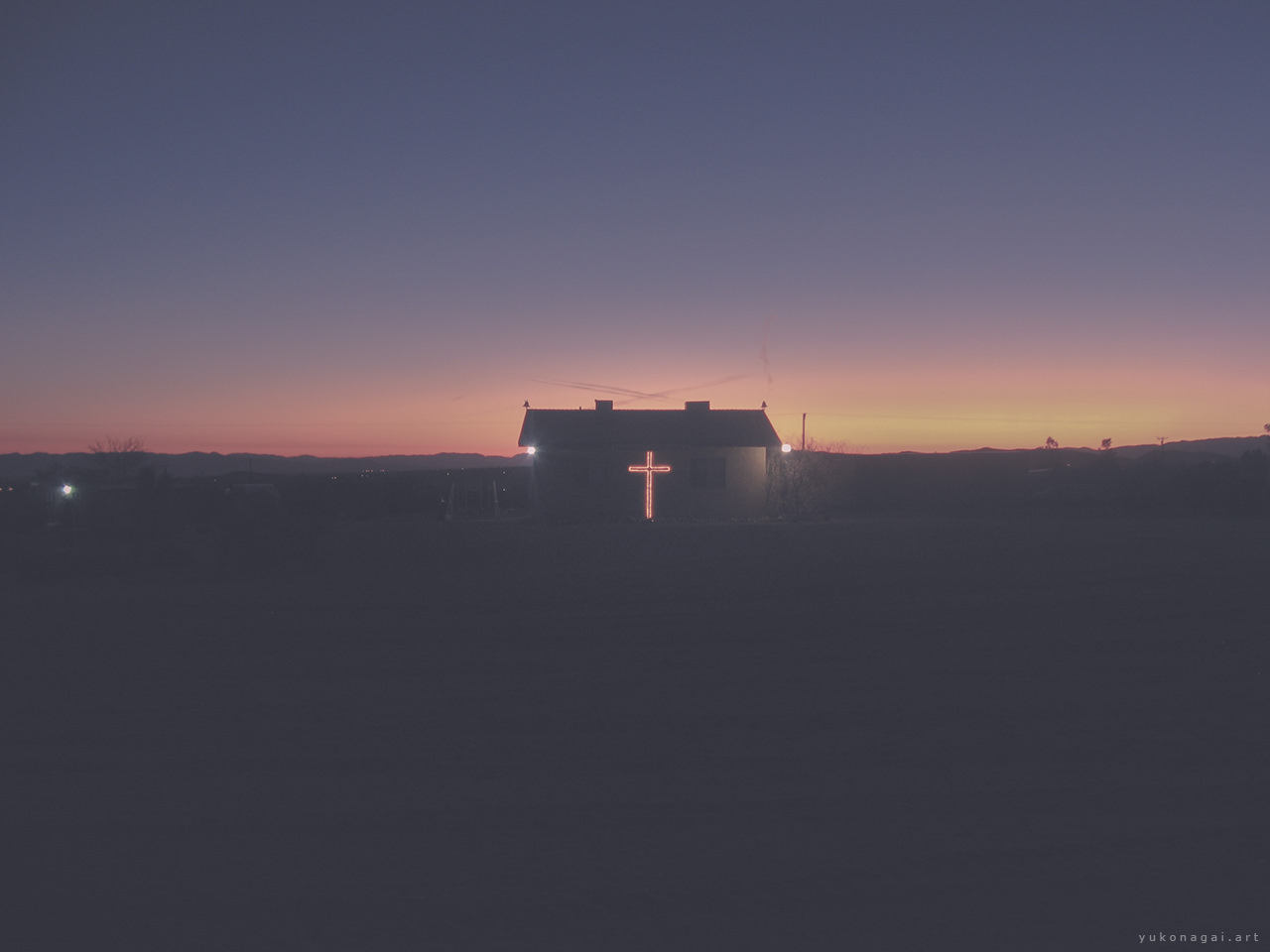 A small church with a lit cross at sunrise.